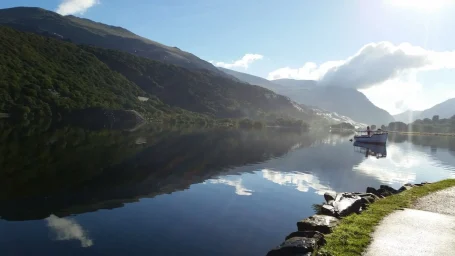 Serene lake surrounded by mountains, reflecting clouds and greenery.